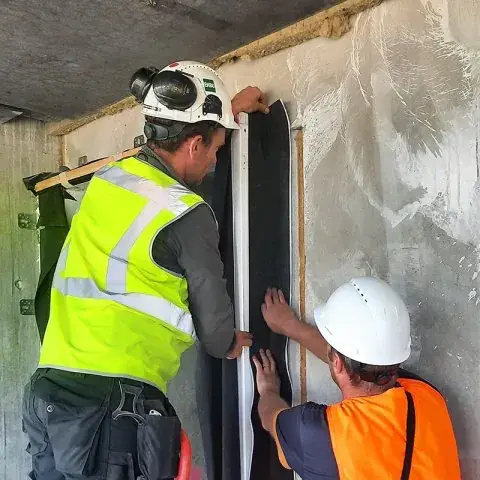 Twee verwerkers brengen een waterkerend membraan aan langs een gevelopening